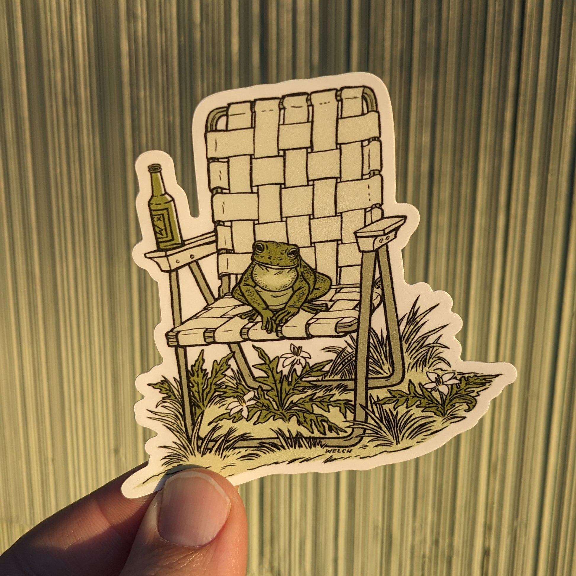 A sticker with an illustration of a frog sitting in a vinyl folding chair. He has a bottle of beer.