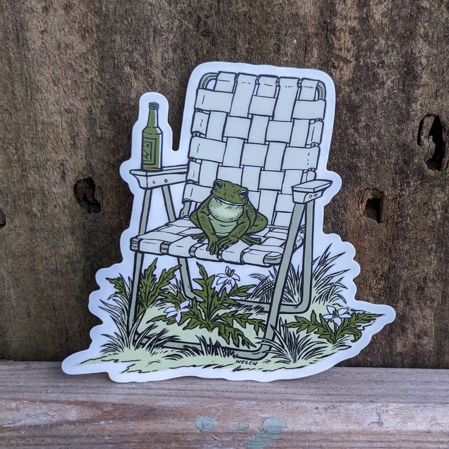 A sticker with an illustration of a frog sitting in a vinyl folding chair. He has a bottle of beer.