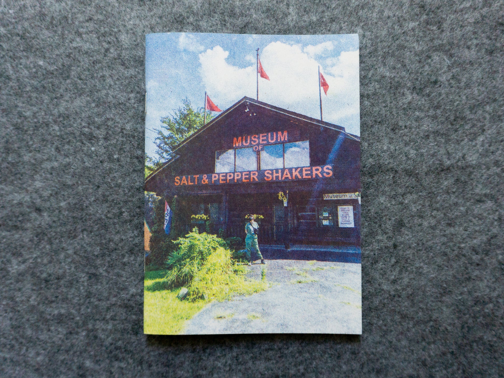 Front cover of zine featuring a woman posed in front of the museum of salt and pepper shakers.